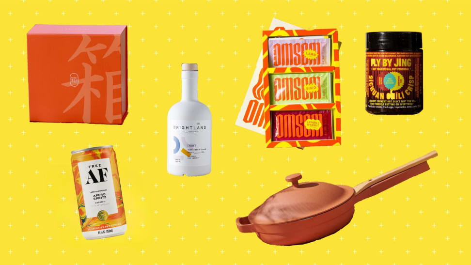 Clockwise from the left: An orange box of Bokksu Japanese snack subscription box, a bottle of Brightland olive oil, a pack of three Southeast Asian sauce kits by Omsom, a jar of Fly By Jing chili crisp, a Terracotta color Always pan, and a can of Free AF Apero Spritz.