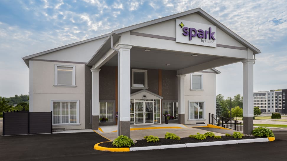Exterior front entrance of a Spark by Hilton hotel with covered driveway, columns, and landscaped entry.