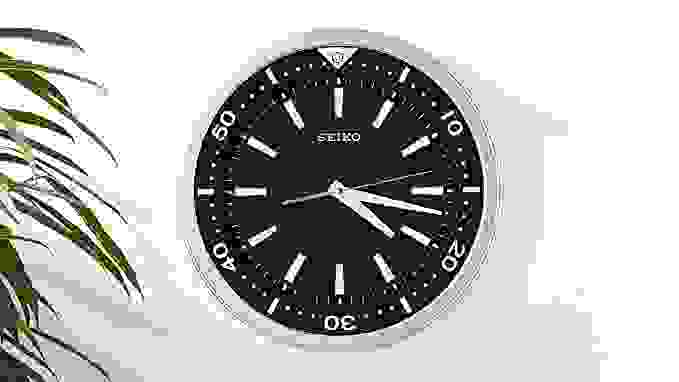A Seiko wall clock hangs on a white wall. Its face is black and it has a silver frame.