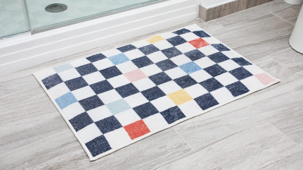 A checkered bath mat sits on a gray floor by a standing shower