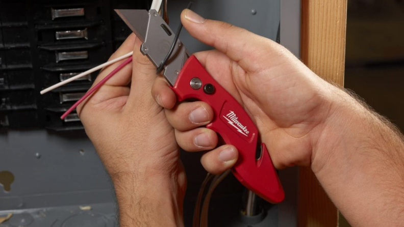 Hands using red utility knife to cut through wires.