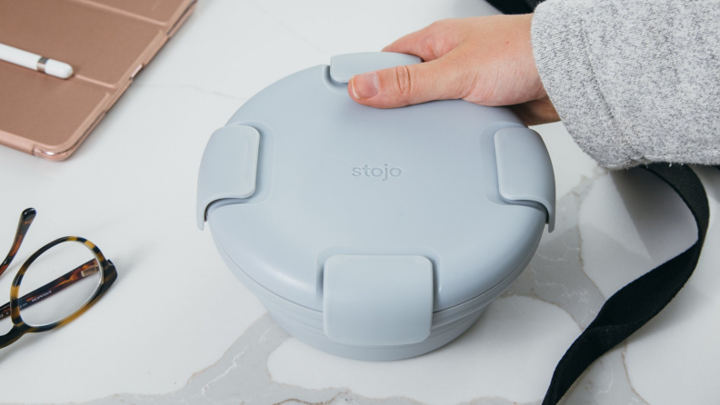 On a desk, a person is holding a pastel blue colored Stojo bowl.