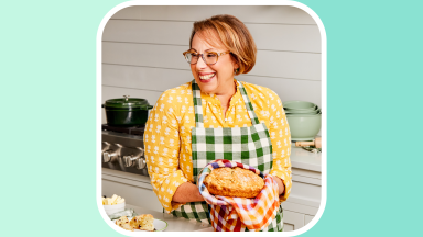A photo of Barbara Costello holding a pie in a kitchen set against a teal background.