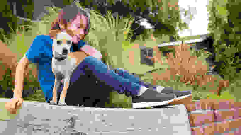 A child sits on a wall with their dog, wearing their Native shoes.