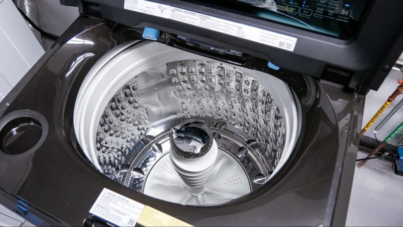 The silver inside of a black washing machine with agitator pole, showing a white garment inside.