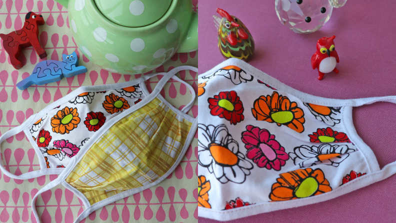 Two face masks with brightly colored flowers laying on a table next to a green teapot.