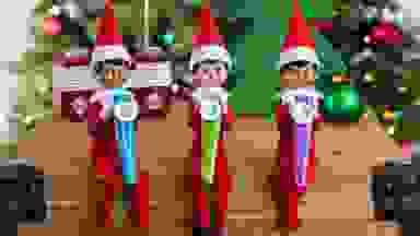 A row of three elves sitting on a shelf playing kazoos.