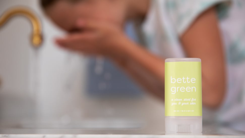 A tube of Bette Green kids' face wash sitting on a counter while a child splashes water on their face in the background.