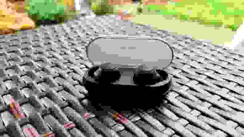 黑色圆形的索尼WF-C500耳塞放在一个开放的盒子里，上面是网格条，背景是绿色的草地。