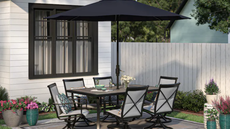 A set of black patio furniture sits in a suburban backyard.