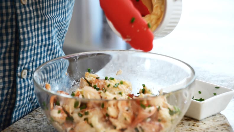 A person is holding a pair of tongs to mix the lobster meal with seasonings in a large bowl.