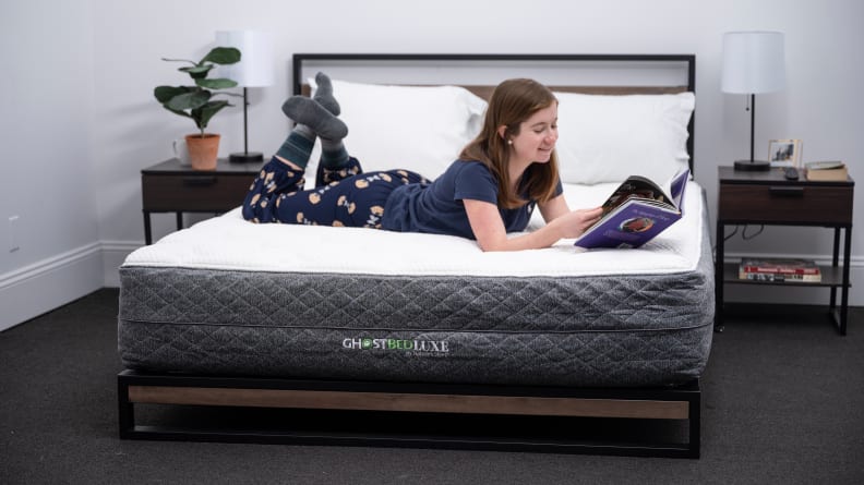 A woman laying down on the GhostBed Luxe while she reads.