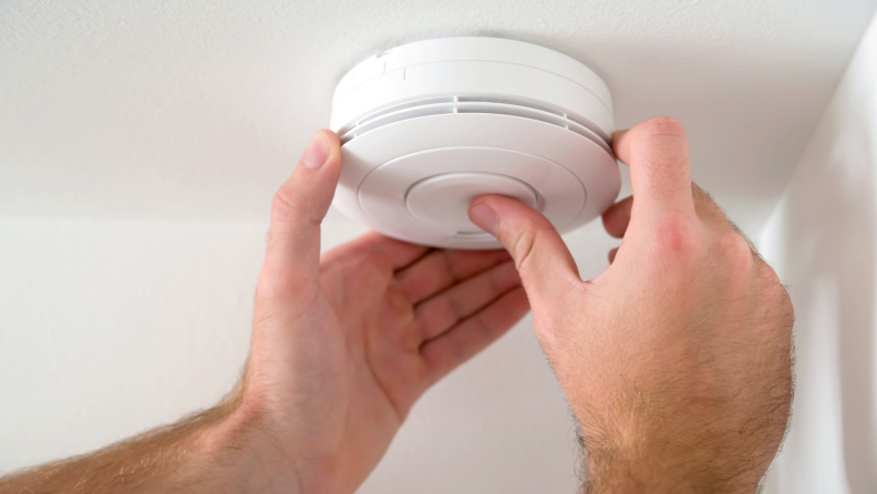 Person fixing smoke detector on ceiling