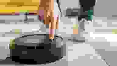 Cropped view of man pointing with finger at robotic vacuum cleaner in living room.