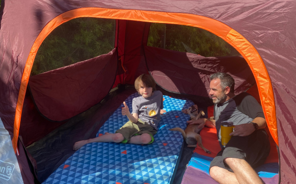 A child, a puppy, and a father recline in a Coleman Skylodge Instant Tent