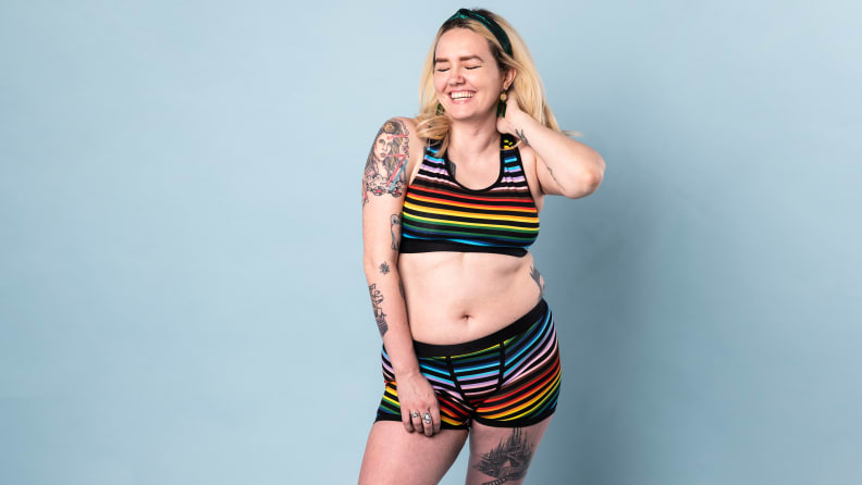 A human wearing TomboyX underwear, against black background.