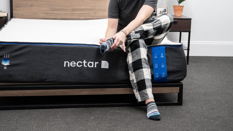 a person sits on the edge of the nectar mattress and puts on socks