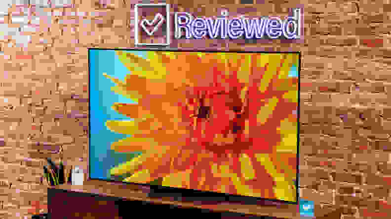 The LG B2 on a wooden table in front of a brick wall with a neon Reviewed sign displaying a flower.