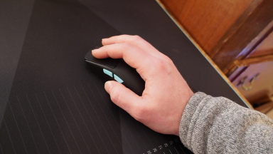 Person uses hand to operate the ROG Harpe Ace Aim Lab mouse on surface.