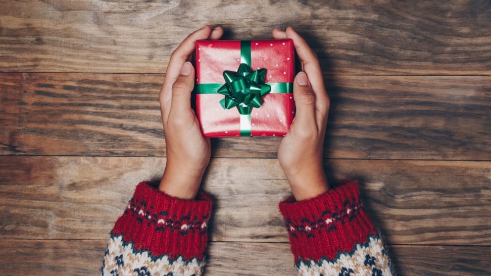 Person wearing holiday sweater holding wrapped gift