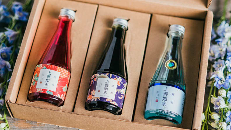 A cardboard box containing three bottles of sake, artfully framed by flowers.
