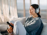 a person sits on a couch, leaned back wearing headphones and meditating