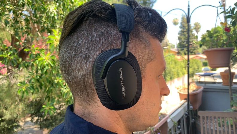 A person pictured in profile wear the Bowers & Wilkins Px7 S2 headphones outdoors with bird feeders and trees in the background.