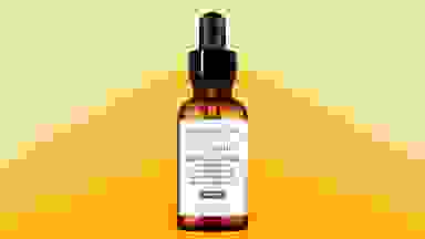 A amber glass bottle of serum in front of a background that's three shades of yellow deepening from top to bottom.