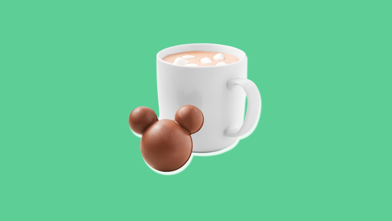 A chocolate sphere with Mickey ears against a white mug of hot chocolate with marshmallows floating in it.