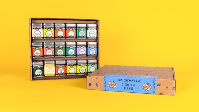 An assortment of spice tins arranged in a cardboard box against a bright yellow background.