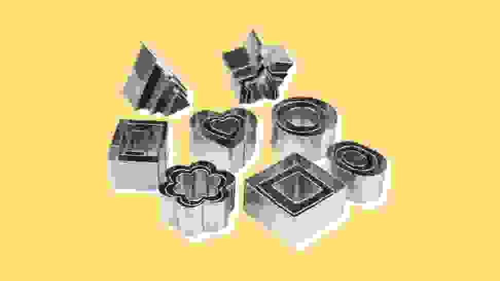 Several different shapes and sizes of stainless steel cookie cutters on yellow background