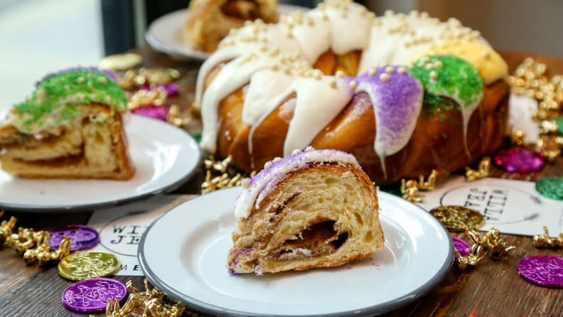 A Willa Jean king cake with decorative necklaces surrounding and three slices separately plated beside it.