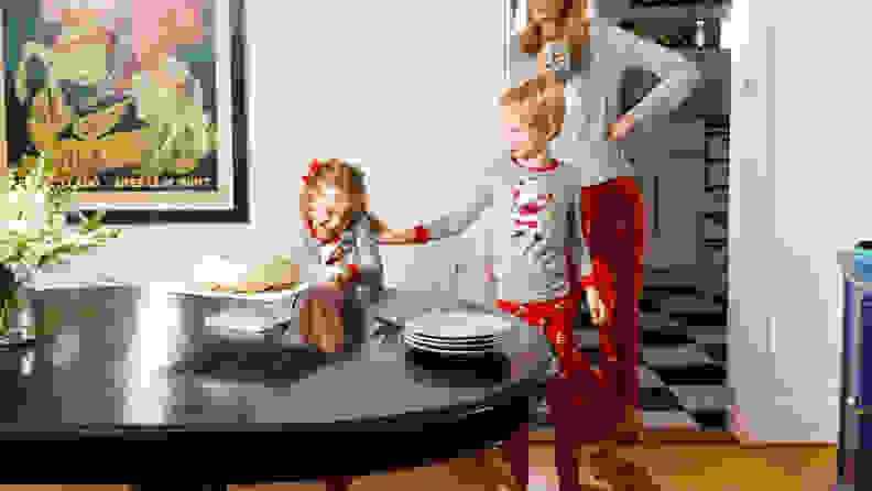 A mom and two kids wearing matching Christmas pajamas in a dining room