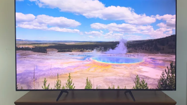 The TCL 5-Series displaying an image of Morning Glory hot spring while sitting on a wooden credenza.