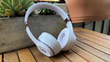 The Beats Solo 4 resting against a stone planter on a wooden table outside.