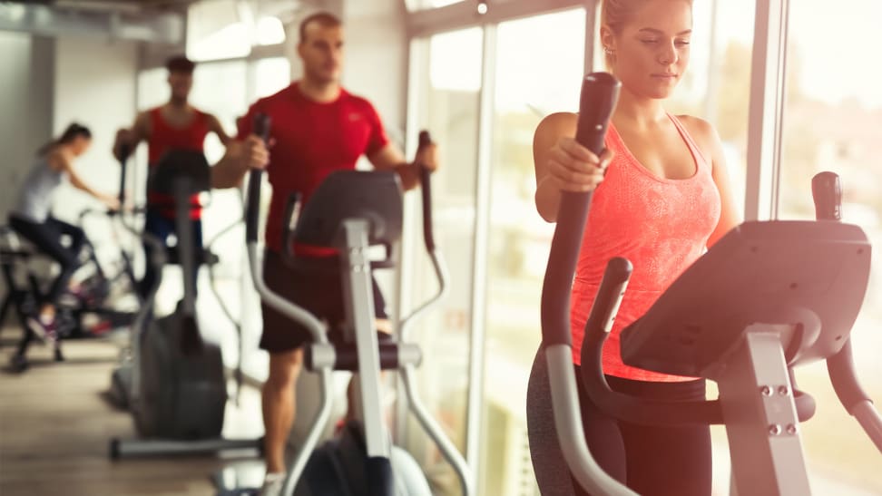 A woman and a man using elliptical machines at the gym.