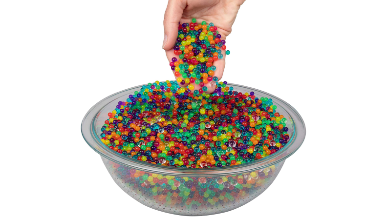 A hand reaches into a bowl of colorful water beads.