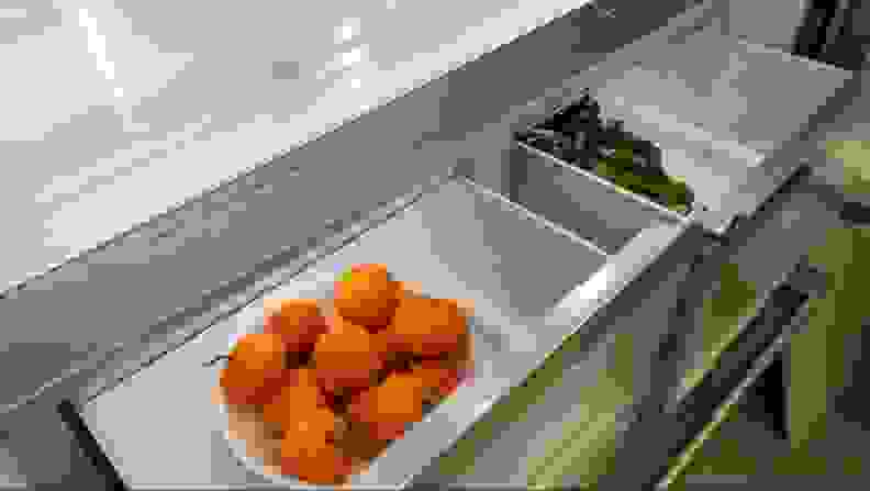 A bowl of oranges and fresh leafy greens found inside a refrigerator's crisper draw.