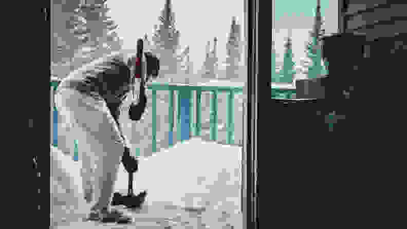 A man stands out on his back porch, shoveling away some heavy snowfall.