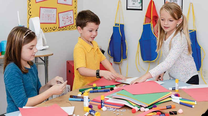Three children sit at a table and make art from colored construction paper