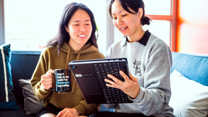 Person holds up a laptop to show the display to someone sitting next to her