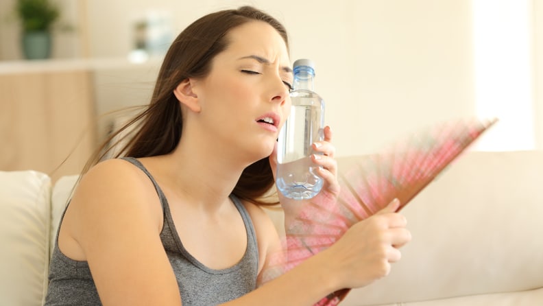 زنی که بیش از حد گرم شده است، در حالی که یک بطری آب را روی صورتش گرفته است، خودش را طرفدار می کند.
