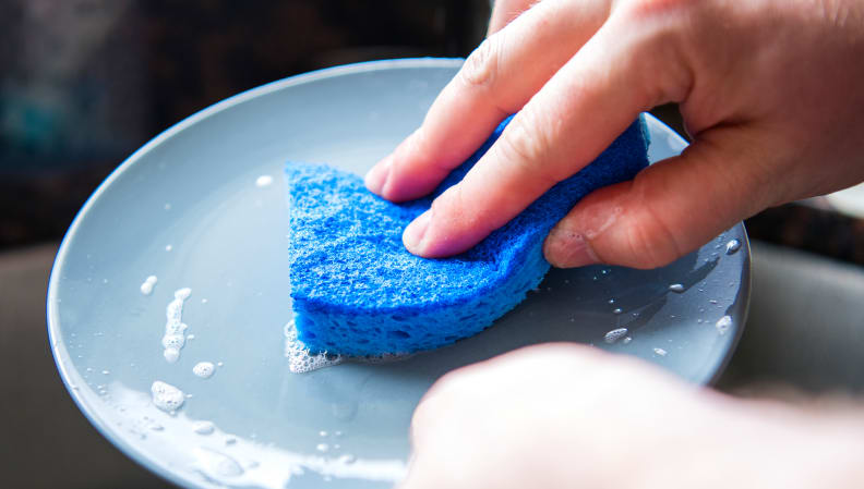 A blue Scotch-Brite non-scratch sponge cleaning a dish