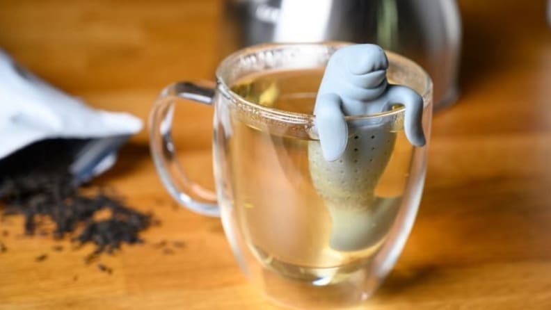 A manatee tea infuser sits on the rim of a glass mug