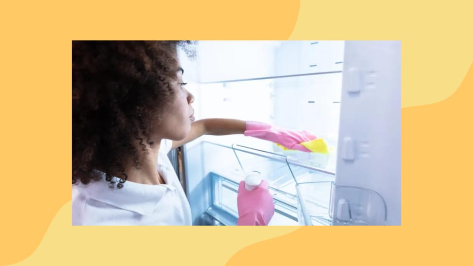 A person wearing rubber gloves wipes down the shelves in a fridge with a cloth