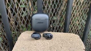 The Bose QuietComfort II earbuds with the carrying case on display in an outdoor setting.
