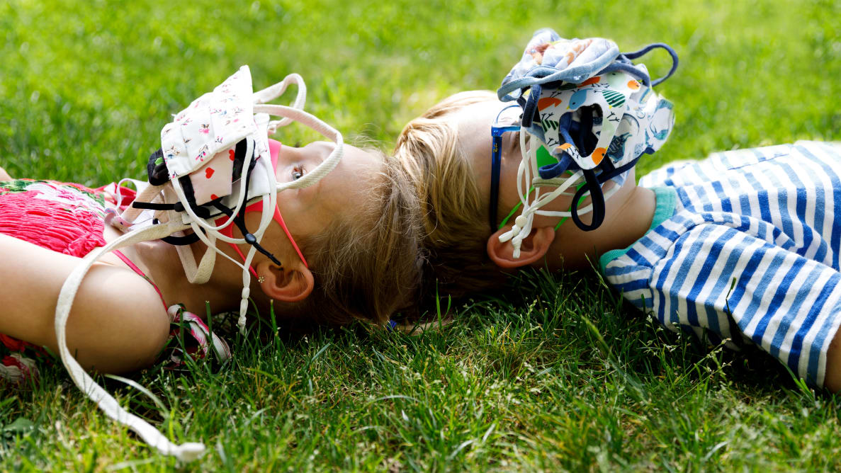 两个小孩躺在草地上，脸上戴着一堆口罩