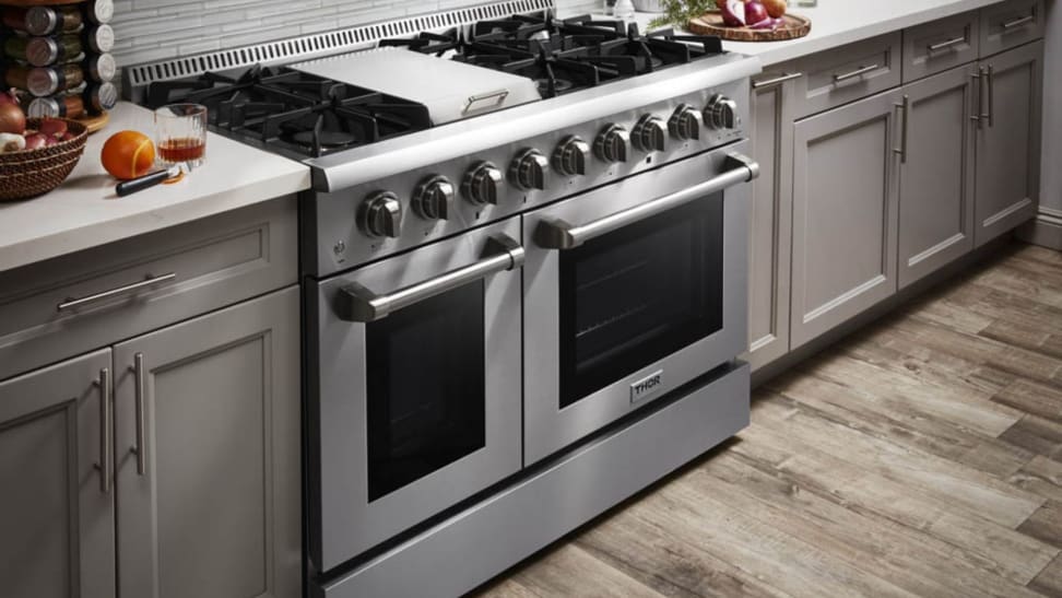 A stainless steel, professional-grade double oven range is brightly lit in a modern looking kitchen.