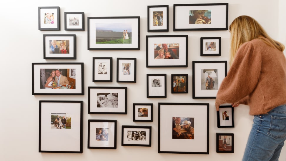 A woman adjusts a photo on a Framebridge gallery wall