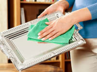 Person using green microfiber cloth to polish silver tray.